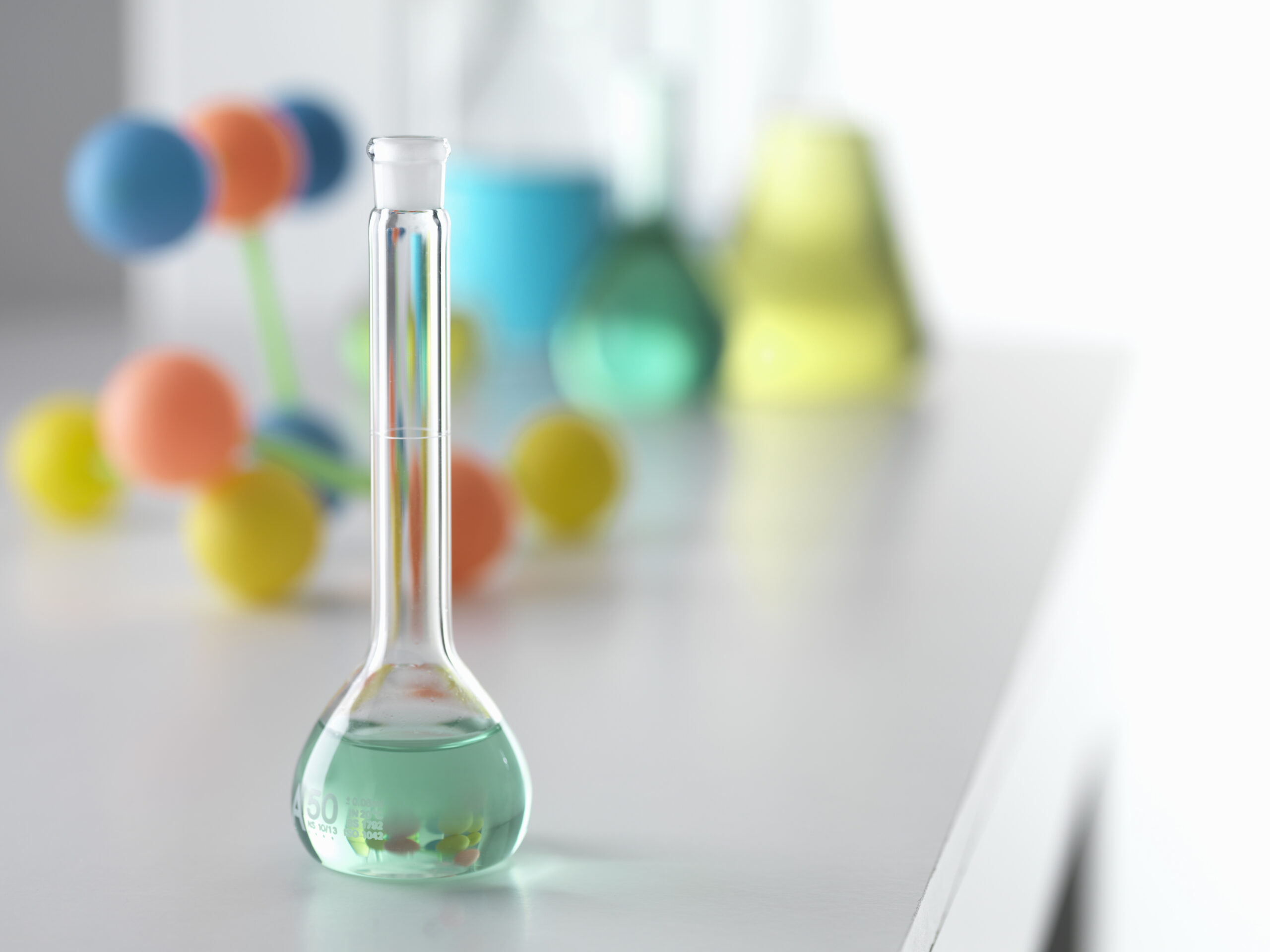 Beaker containing solution from chemical experiment with molecular model in background on lab bench