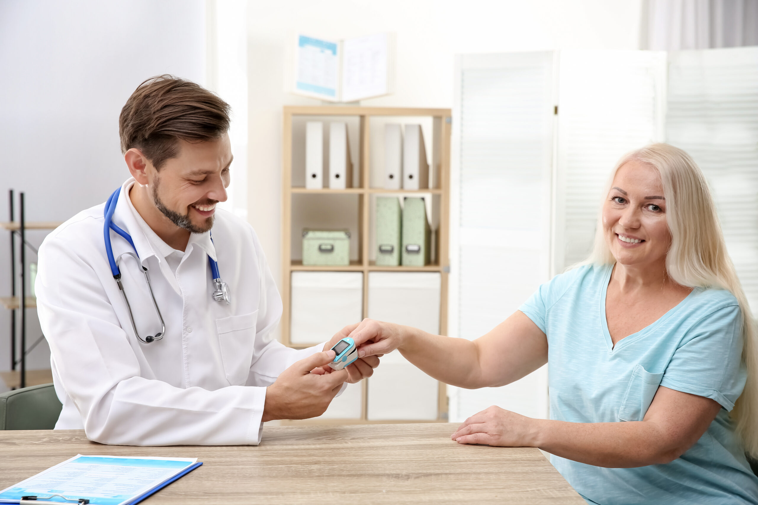 Doctor checking mature woman’s pulse with medical device in hospital