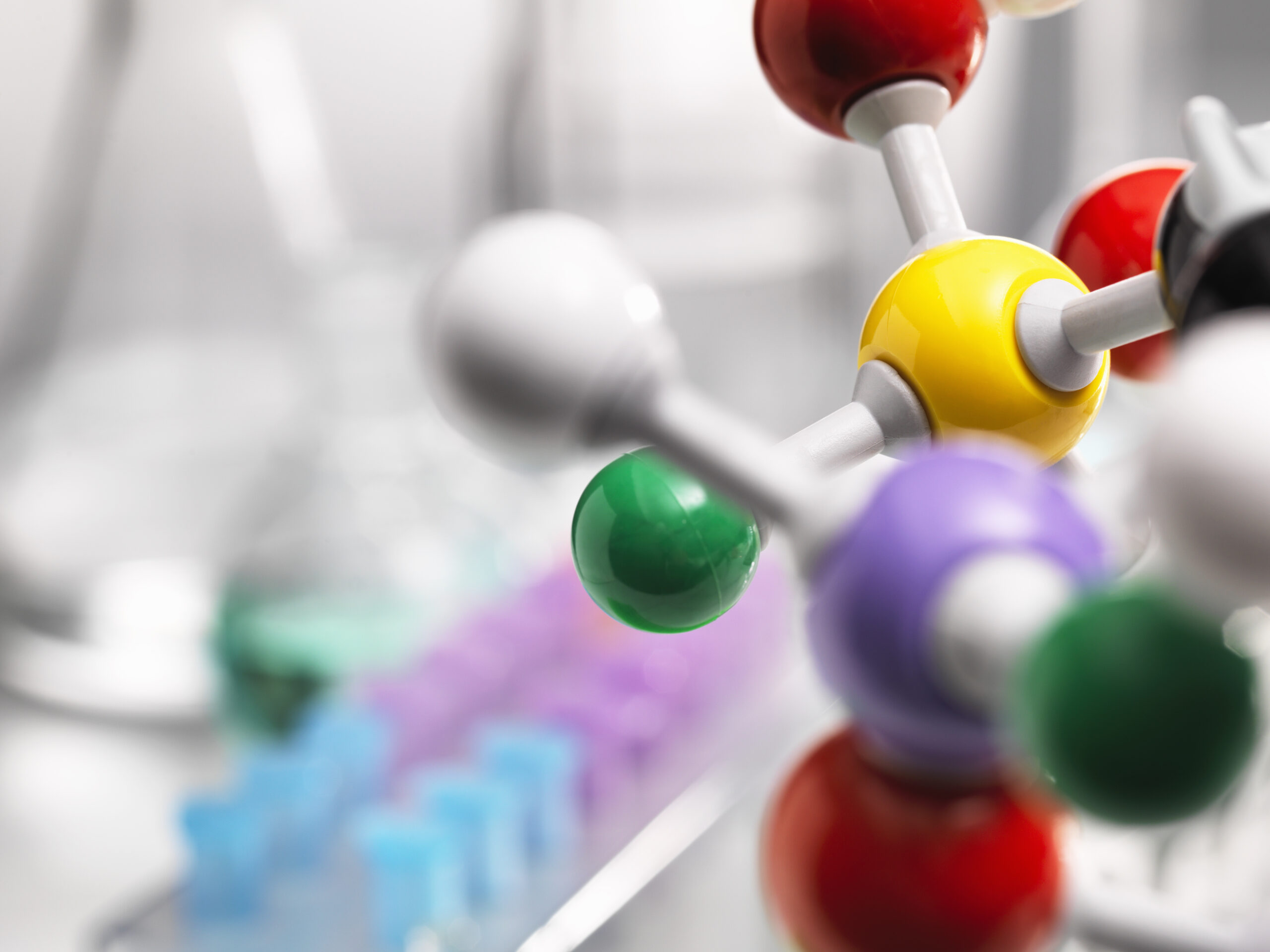 A molecular model of a chemical formula with laboratory equipment in the background