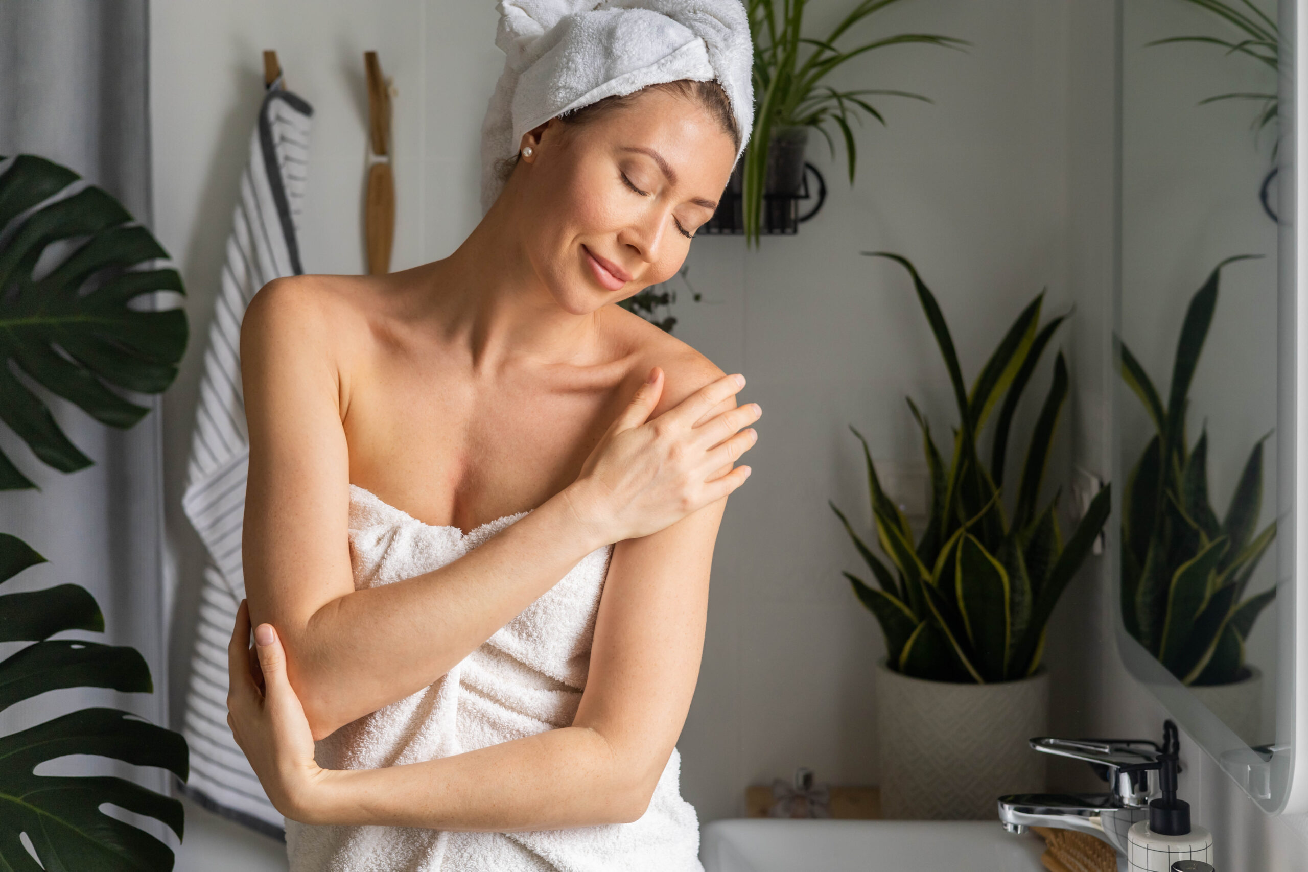 A young beautiful woman in a white terry towel admires herself in front of a mirror in her bathroom.
