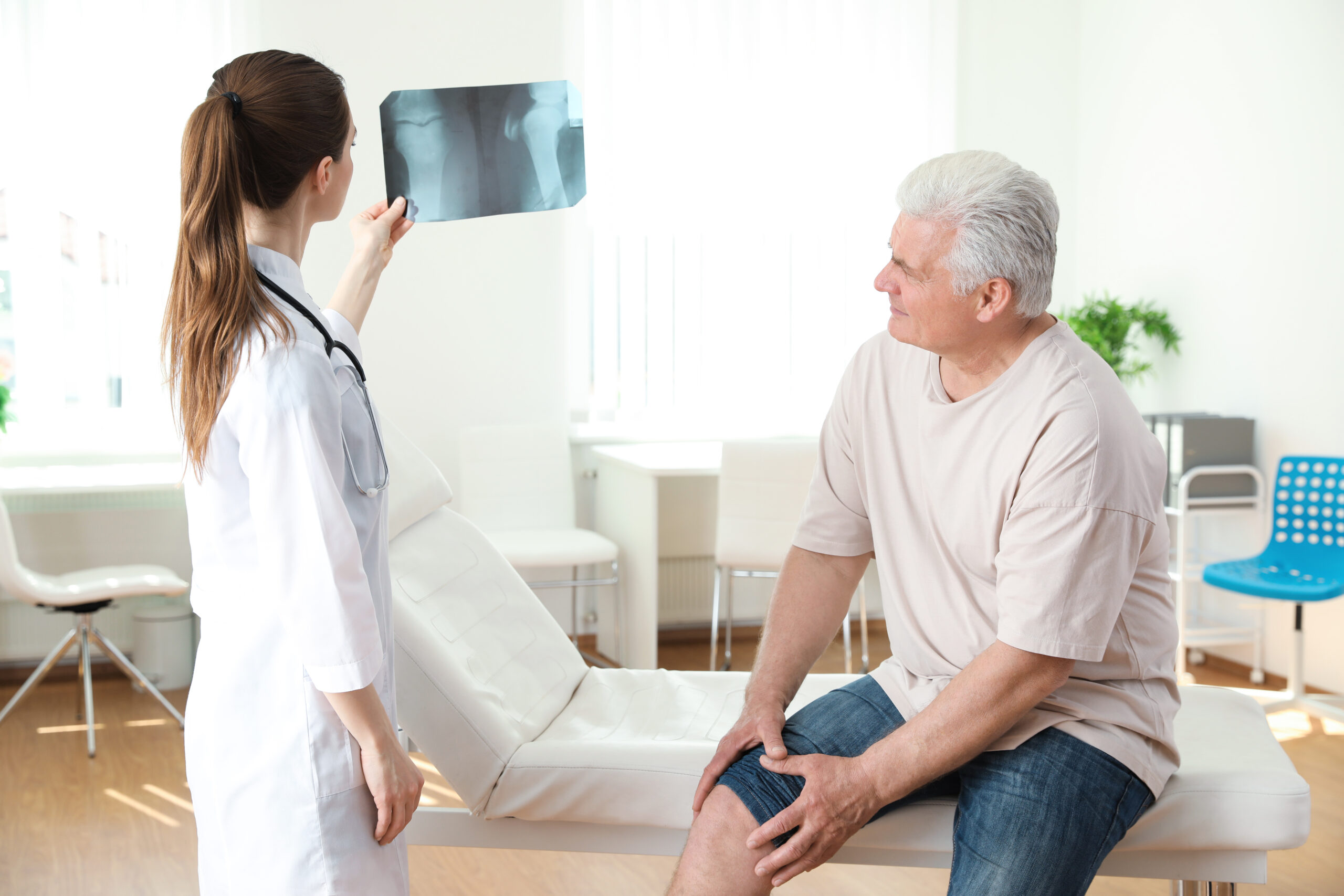 Young doctor with X-ray and senior patient in clinic. Knee problem